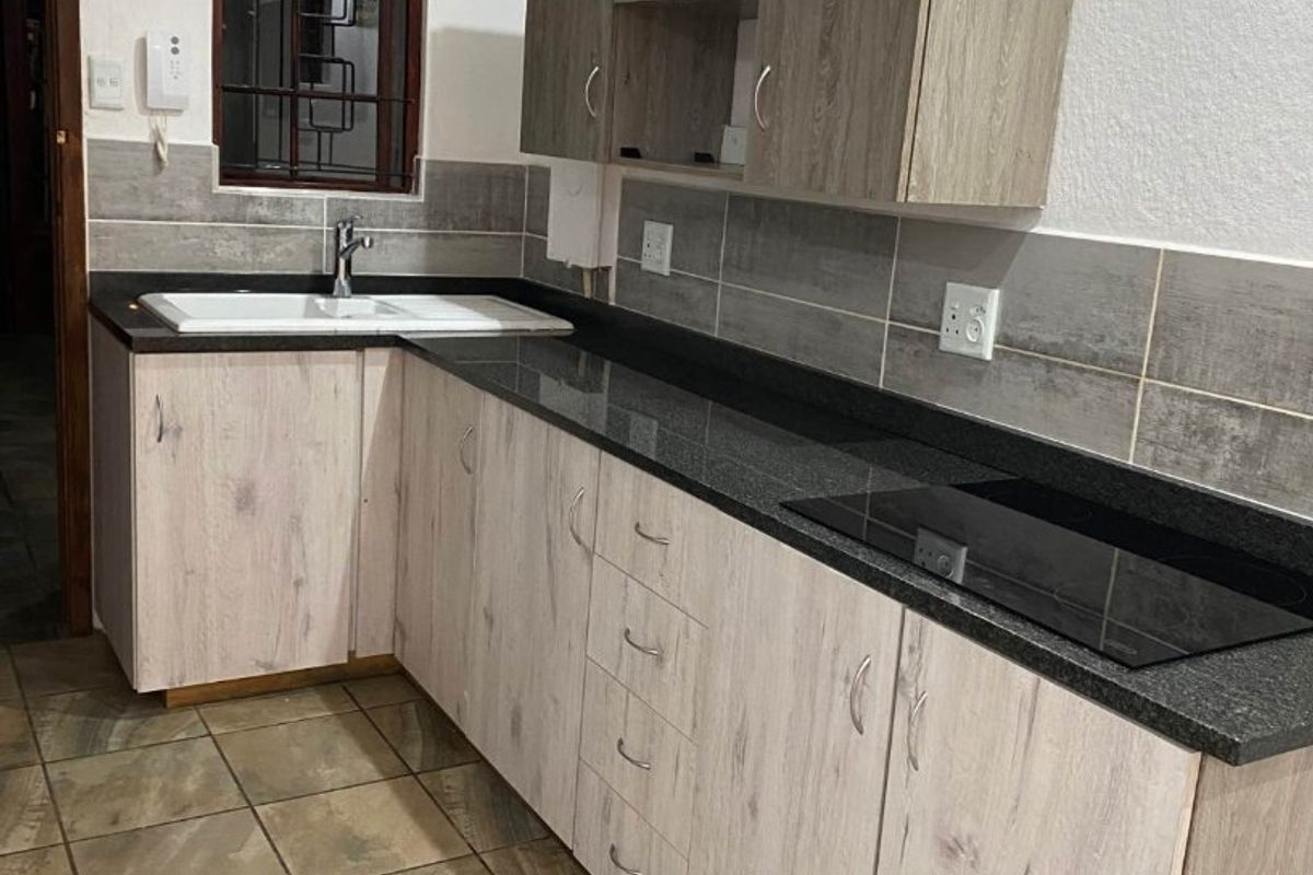 A functional kitchen featuring light wood-look cabinetry, dark granite countertops, a built-in induction hob, and tiled flooring with a neutral backsplash.