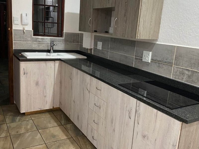 A functional kitchen featuring light wood-look cabinetry, dark granite countertops, a built-in induction hob, and tiled flooring with a neutral backsplash.