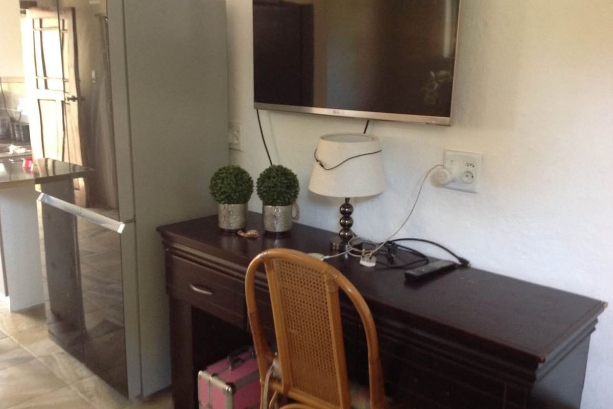 A living area featuring a wall-mounted television and electrical points, adjacent to a kitchen space.