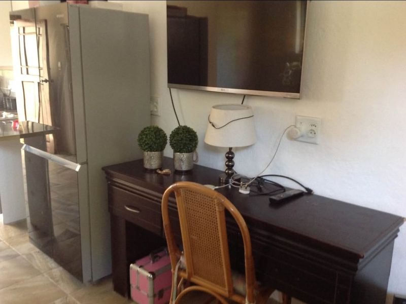 A living area featuring a wall-mounted television and electrical points, adjacent to a kitchen space.
