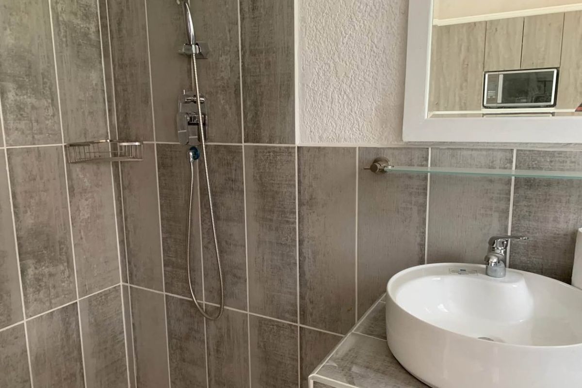 A modern bathroom featuring a vessel sink, tiled shower enclosure with a handheld shower head, and a wall-mounted mirror.