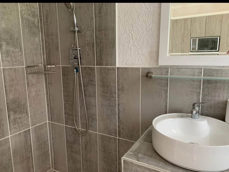 A modern bathroom featuring a vessel sink, tiled shower enclosure with a handheld shower head, and a wall-mounted mirror.