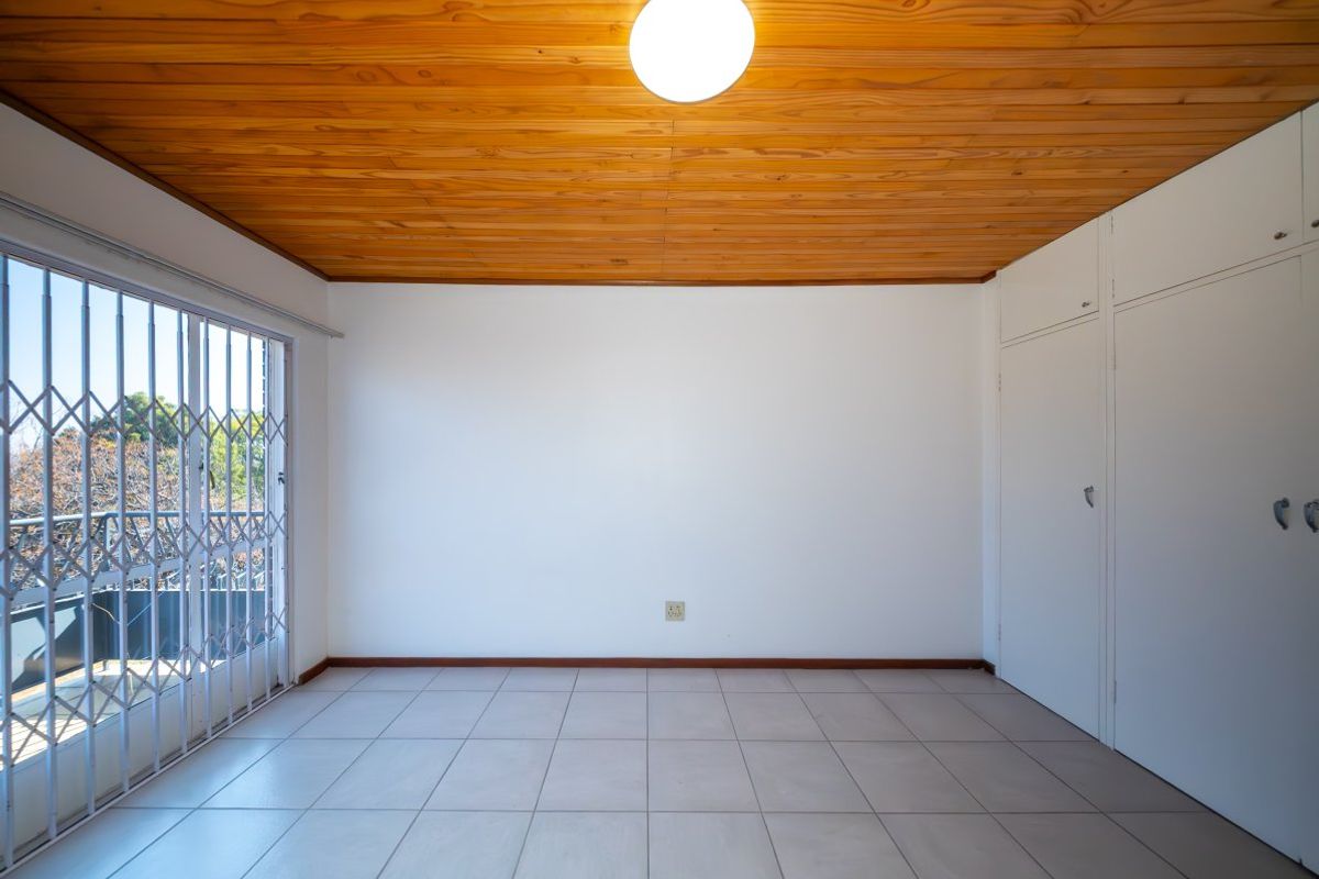 An empty bedroom featuring tiled flooring, built-in cupboards, and a distinctive timber tongue and groove ceiling, with access to a balcony via a security gate.