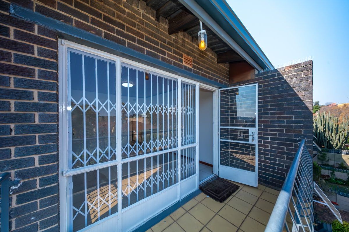 A private balcony featuring brick walls, tiled flooring, a metal safety railing, and a secure entrance gate leading into the apartment.