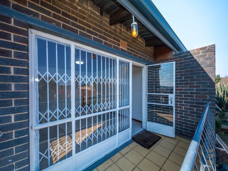 A private balcony featuring brick walls, tiled flooring, a metal safety railing, and a secure entrance gate leading into the apartment.