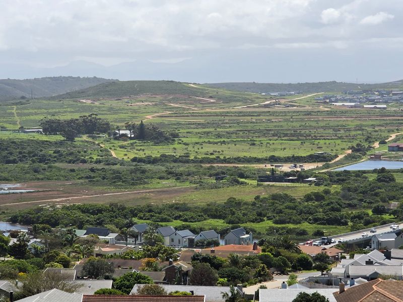 An elevated panoramic view overlooking a coastal landscape with rolling green hills, wetlands, and residential housing developments.