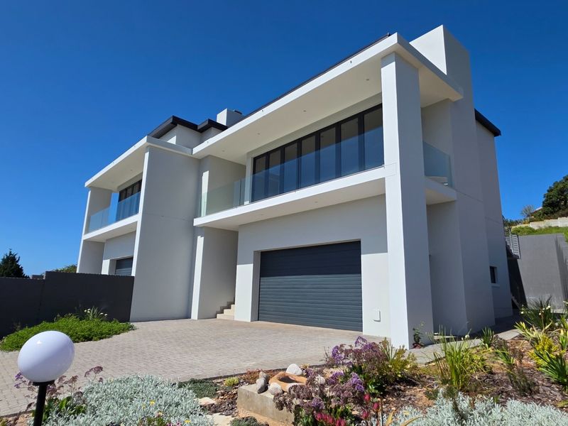 Modern double-story residence featuring a paved driveway, integrated double garage, and upper-level balconies with glass balustrades.