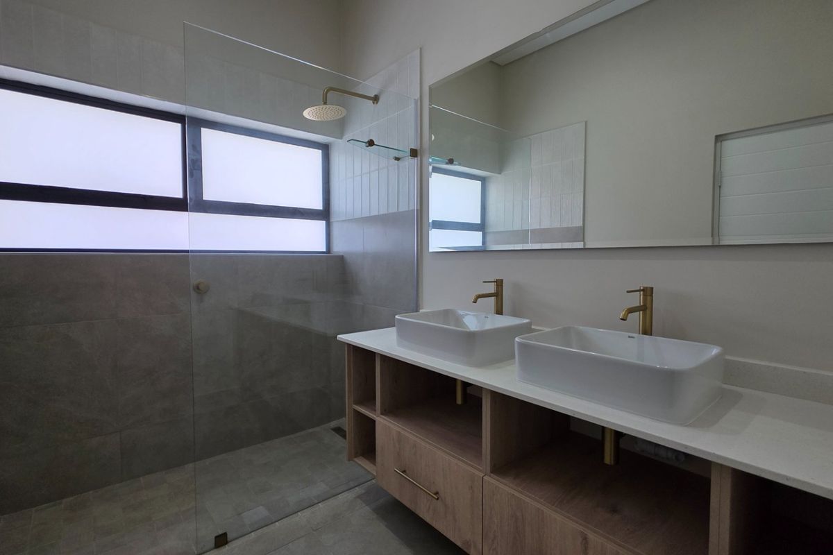 Modern bathroom featuring a double vanity with vessel sinks, brass fixtures, and a spacious walk-in shower with a frameless glass screen.