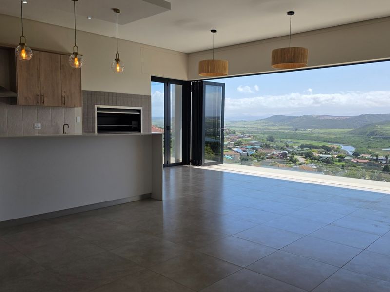Modern open-plan kitchen and living area featuring sleek cabinetry, built-in braai, and expansive stacking doors opening to panoramic valley and river views.