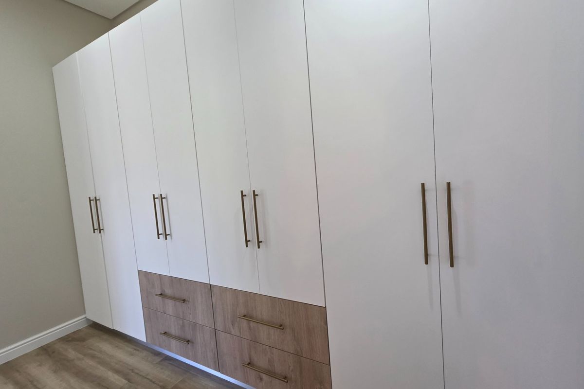 A modern bedroom featuring extensive floor-to-ceiling built-in cupboards with a clean white and wood-grain finish, complemented by durable laminate flooring.