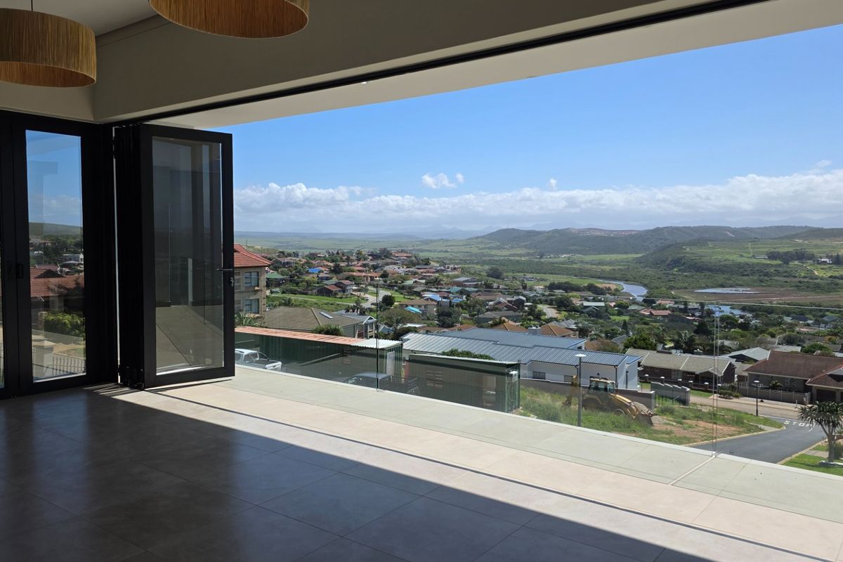 Spacious living area featuring large bi-fold doors opening to a glass balustrade balcony with expansive panoramic views of the surrounding landscape.