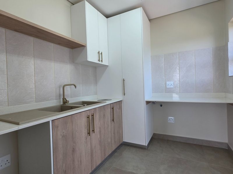 A modern, clean laundry room featuring built-in cabinetry, stone countertops, a double sink, and dedicated plumbing connections for appliances.