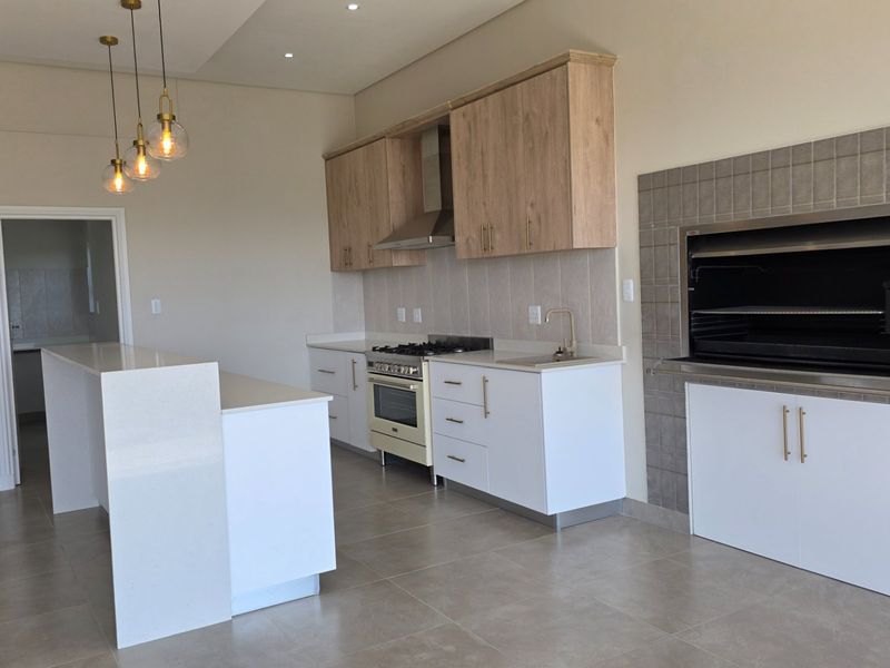 Modern open-plan kitchen featuring a built-in braai, quartz countertops, gas stove, and a central island, finished with neutral tiling and contemporary cabinetry.