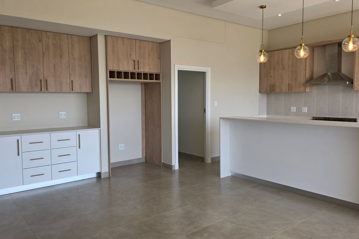 Modern kitchen featuring light wood cabinetry, stone countertops, a breakfast bar, and integrated extractor fan, finished with neutral tiled flooring.