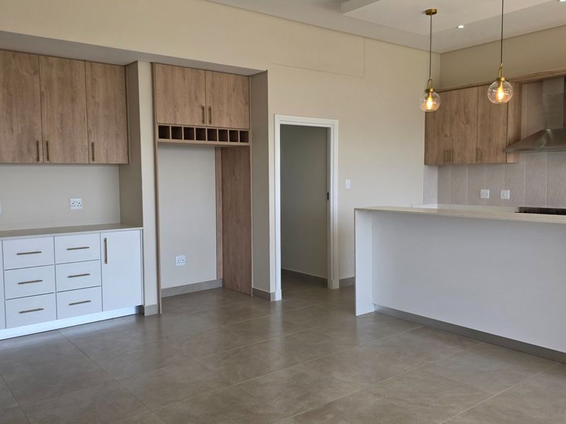 Modern kitchen featuring light wood cabinetry, stone countertops, a breakfast bar, and integrated extractor fan, finished with neutral tiled flooring.