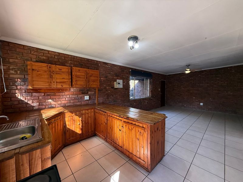 Open plan kitchen and living area featuring exposed brick walls, tiled flooring, and wooden cabinetry with a stainless steel sink.