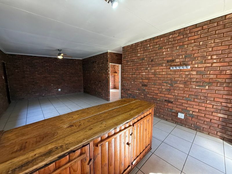 Spacious open-plan living area featuring rustic exposed brick walls, neutral tiled flooring, and a built-in wooden breakfast bar.