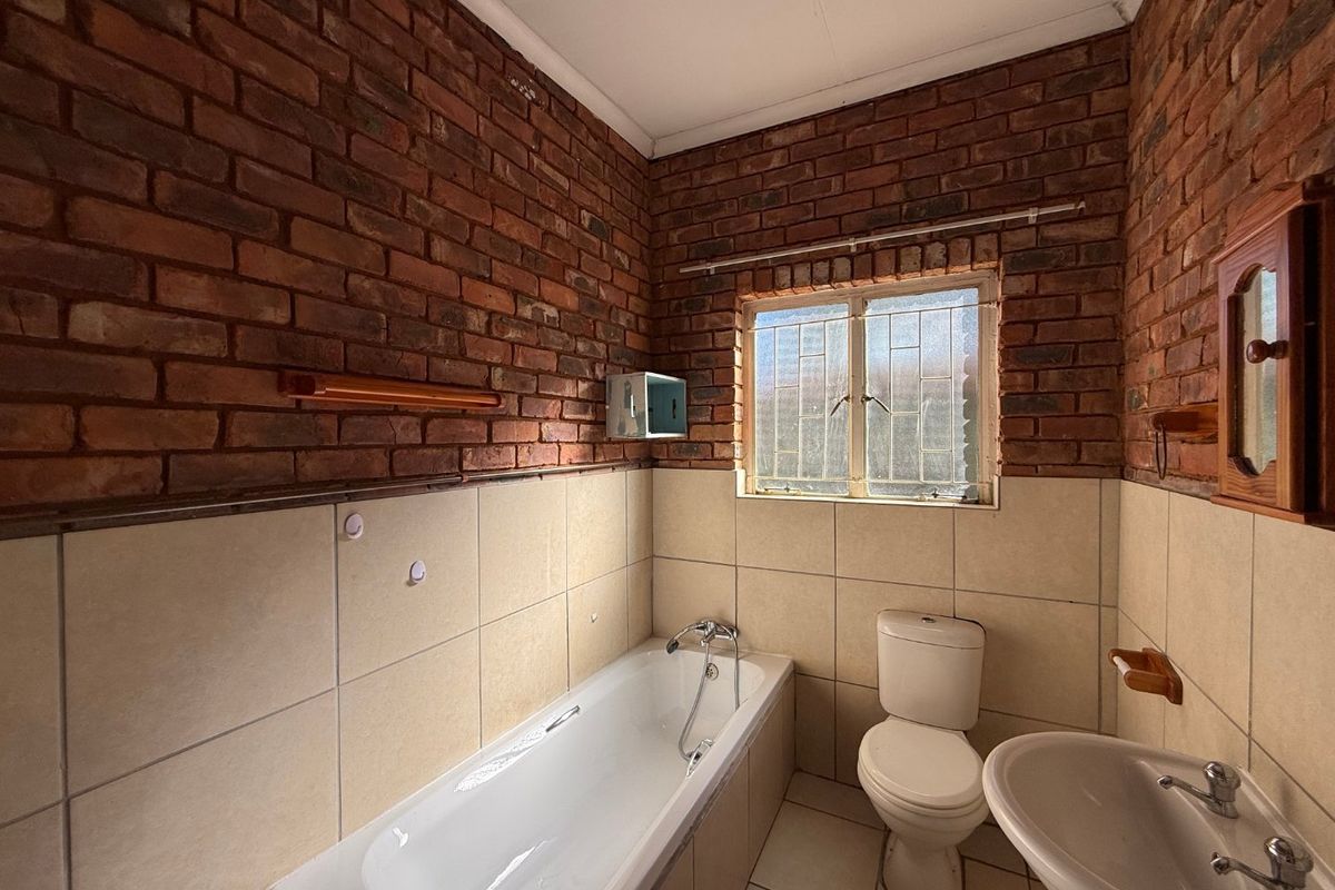 A functional bathroom featuring exposed brick walls, a standard bathtub, toilet, and washbasin, offering a rustic aesthetic with potential for modern updates.