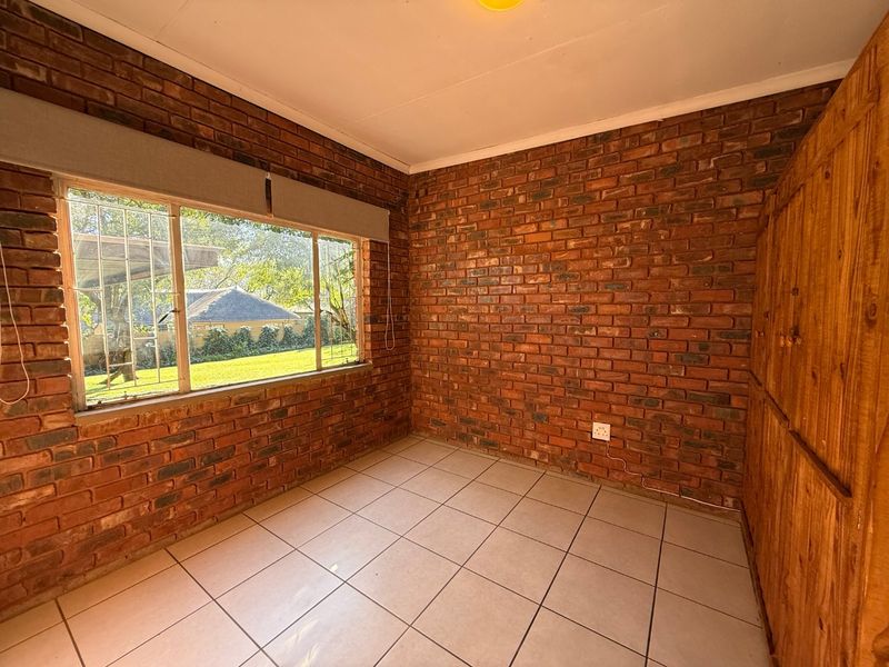 A bright, empty bedroom featuring exposed brick walls, tiled flooring, and built-in wooden cupboards, offering a blank canvas for personalization.