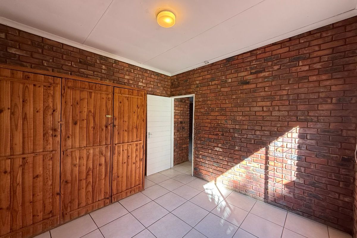 A bedroom featuring exposed brick walls, tiled flooring, and built-in wooden cupboards, offering a rustic aesthetic ready for personalization.