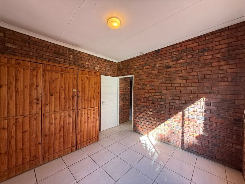 A bedroom featuring exposed brick walls, tiled flooring, and built-in wooden cupboards, offering a rustic aesthetic ready for personalization.