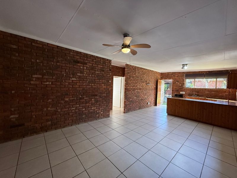 Spacious open-plan living and kitchen area featuring exposed brick walls, tiled flooring, and a functional kitchen island with timber cabinetry.