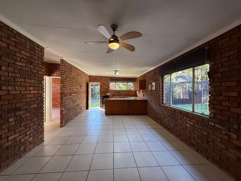Spacious open-plan living and kitchen area featuring exposed brick walls, tiled flooring, and a ceiling fan, offering a blank canvas for renovation.