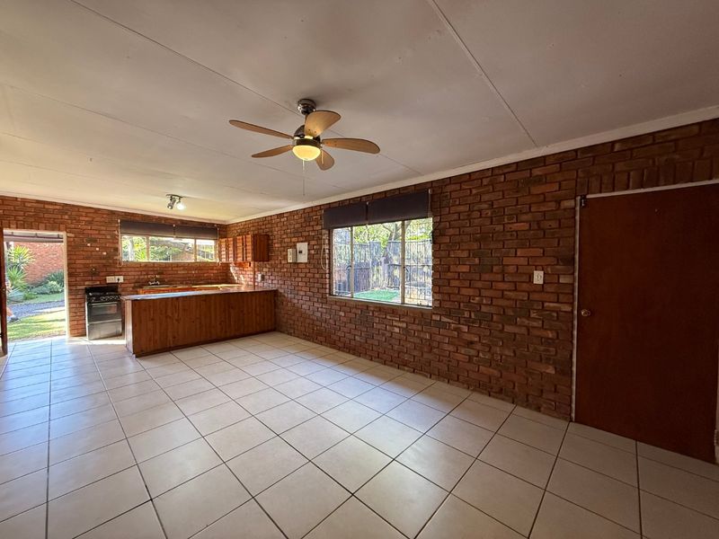 Spacious open-plan living and kitchen area featuring exposed brick walls, ceramic floor tiles, and a functional kitchen layout with a breakfast bar.