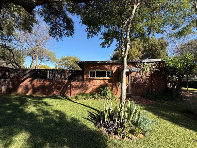 A rear view of the brick house featuring a landscaped garden, mature trees, and a combination of precast concrete and timber boundary fencing.