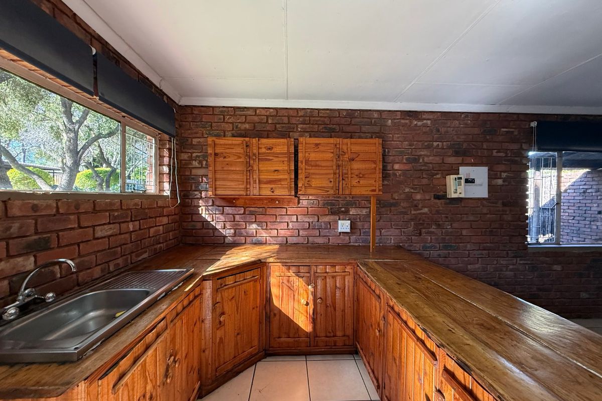 A rustic kitchen featuring exposed brick walls, wooden cabinetry, and wooden countertops with a stainless steel sink and tiled flooring.