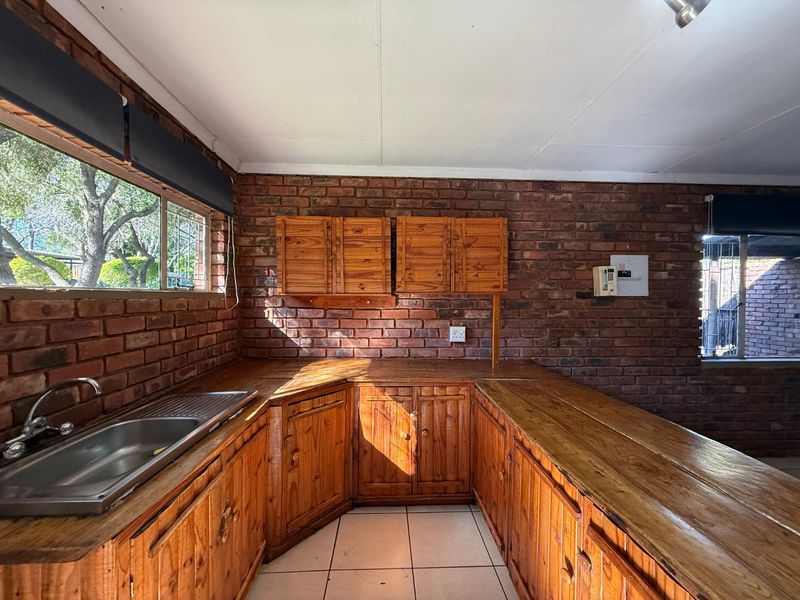 A rustic kitchen featuring exposed brick walls, wooden cabinetry, and wooden countertops with a stainless steel sink and tiled flooring.