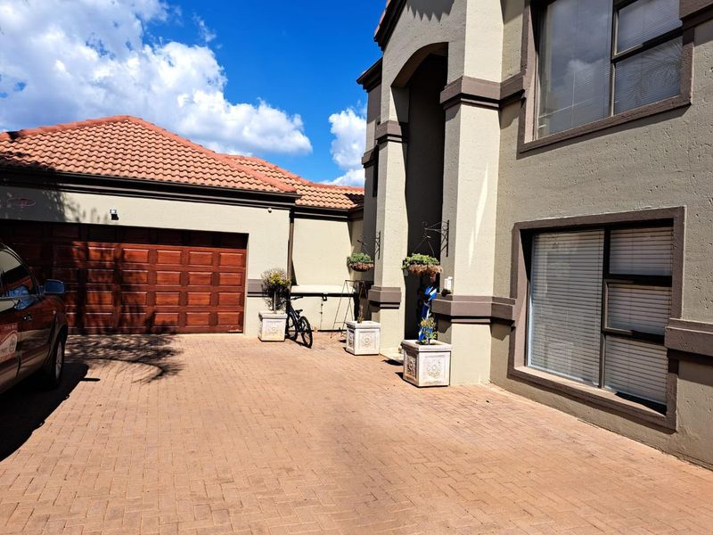 Front elevation of a modern house featuring a paved driveway, double wooden garage door, and tiled roof with a covered entrance.