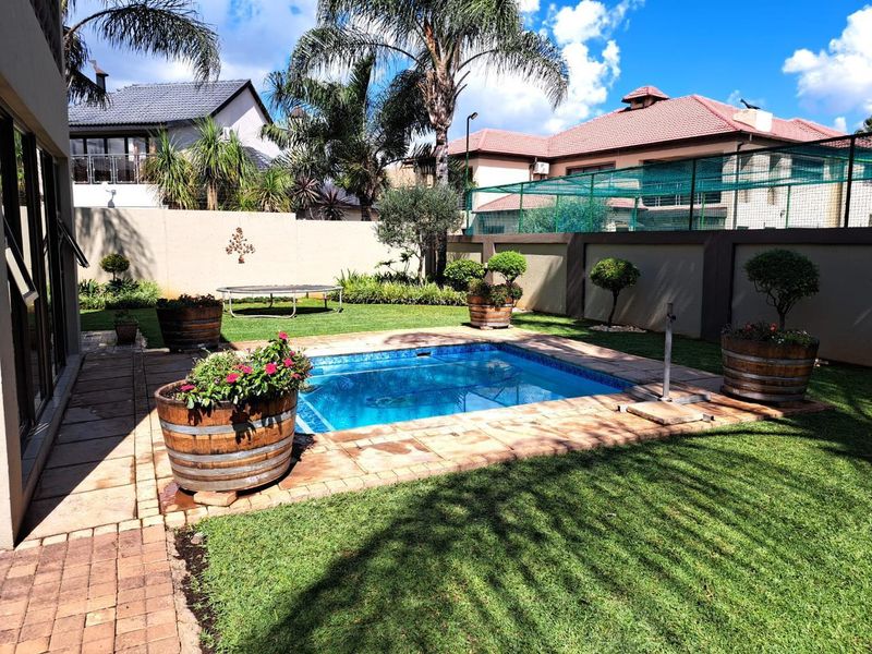 A well-maintained backyard featuring a swimming pool with paved surround, manicured lawn, and high boundary walls for privacy.