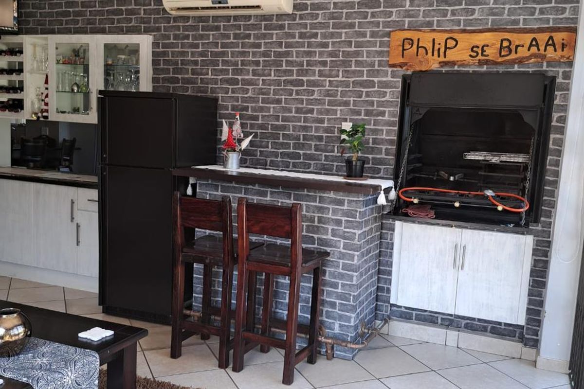 Living area featuring a built-in braai, brick-effect feature wall, tiled flooring, and a wall-mounted air conditioning unit.