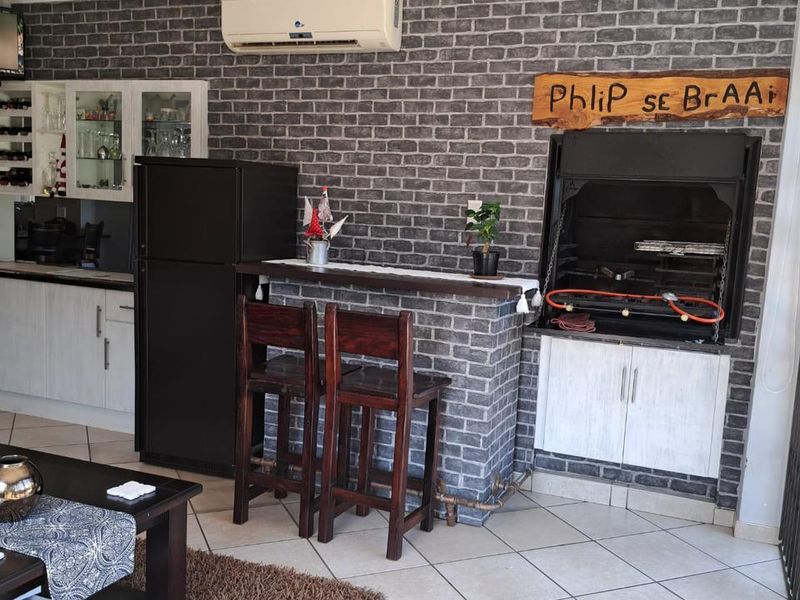Living area featuring a built-in braai, brick-effect feature wall, tiled flooring, and a wall-mounted air conditioning unit.