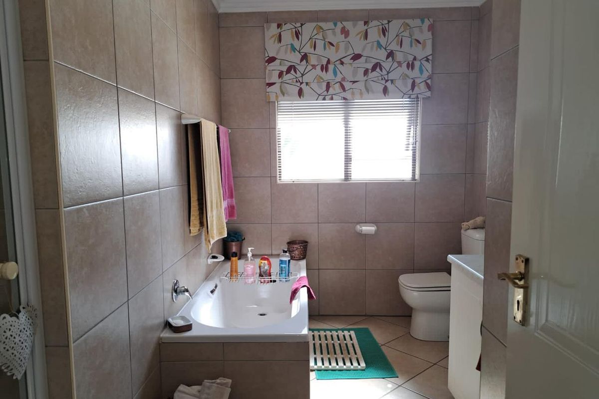 A functional bathroom featuring a built-in bathtub, toilet, and vanity cabinet with neutral wall and floor tiling.