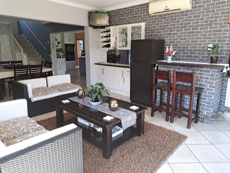 Open-plan living area featuring a brick accent wall, built-in bar, tiled flooring, and an integrated staircase leading to the upper level.