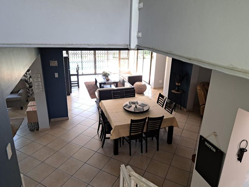 An elevated view of an open-plan living and dining area featuring tiled flooring and sliding glass doors leading to an outdoor space.