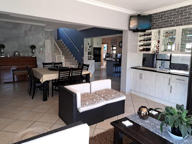 Spacious open-plan living and dining area featuring tiled floors, a built-in bar with wine storage, and a staircase leading to the upper level.