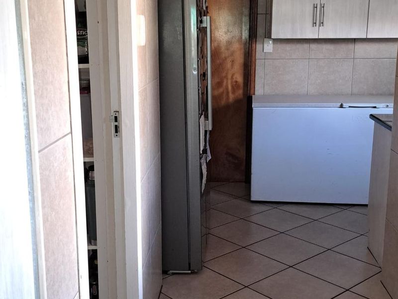 A functional scullery or utility area featuring tiled flooring, built-in cabinetry, and a pantry cupboard, providing additional storage and prep space.