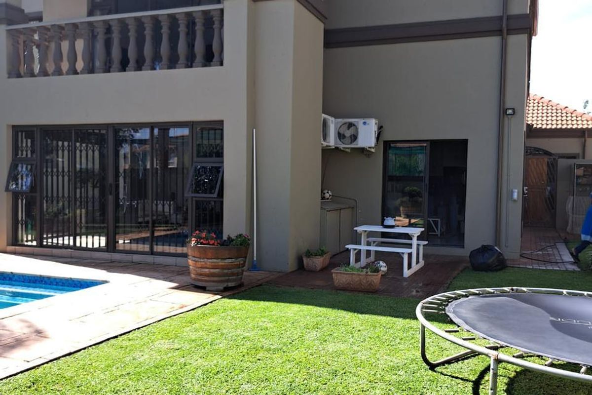 Rear view of a two-story house featuring a swimming pool, a paved patio area, and an upper-level balcony with a balustrade.