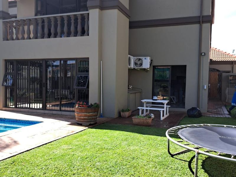 Rear view of a two-story house featuring a swimming pool, a paved patio area, and an upper-level balcony with a balustrade.