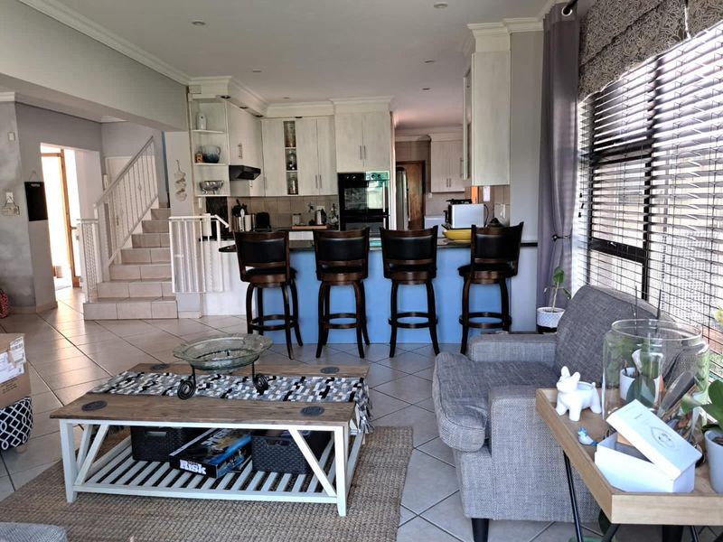 An open-plan living and kitchen area featuring tiled floors, a central kitchen island with breakfast bar seating, and an integrated staircase.