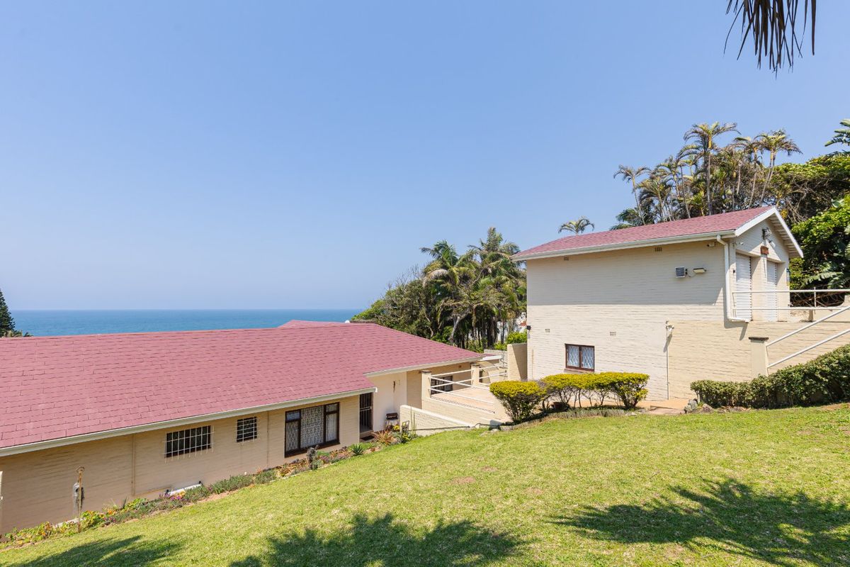 Rear view of the property featuring a multi-level brick structure with pitched roofs, set against a coastal backdrop with a well-maintained lawn.