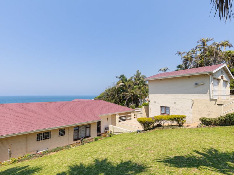 Rear view of the property featuring a multi-level brick structure with pitched roofs, set against a coastal backdrop with a well-maintained lawn.