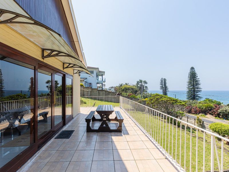 Spacious tiled patio featuring a metal balustrade and sliding glass doors, offering scenic coastal views and an ideal space for outdoor relaxation.
