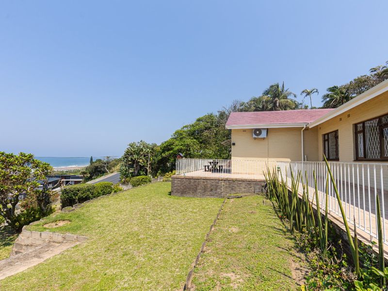 Rear view of the property featuring a tiled patio with metal balustrades, brick retaining wall, and elevated views towards the coastline.