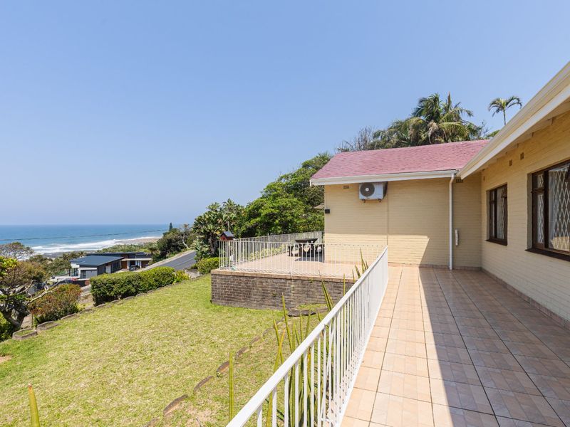 Spacious tiled patio area featuring a metal balustrade, overlooking the garden with scenic coastal views.