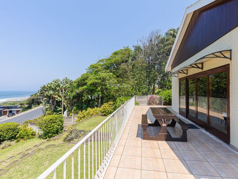 Spacious tiled patio featuring a metal balustrade and sliding glass doors, offering elevated views of the surrounding landscape and coastline.