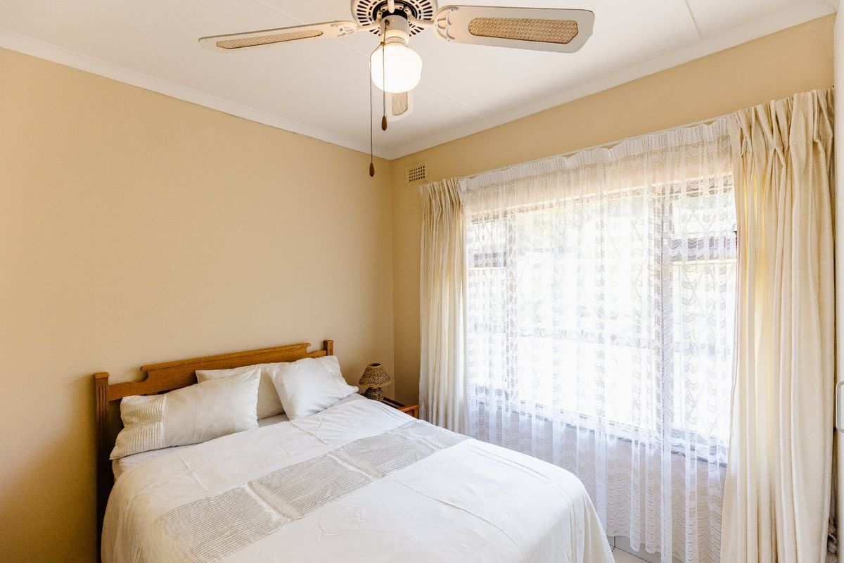 A well-lit bedroom featuring a ceiling fan and large window with curtain rails, offering a neutral and comfortable living space.